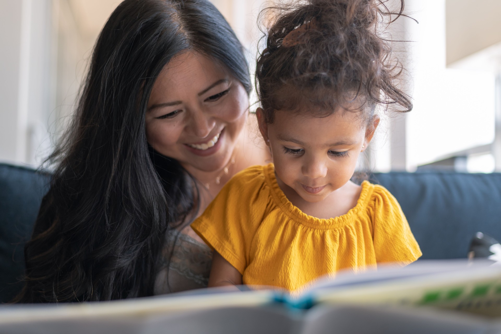 Adorable mixed race toddler reading book with her mother